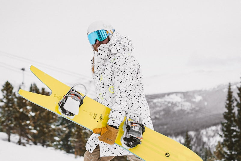 man in white and green jacket and brown pants holding yellow snowboard during daytime